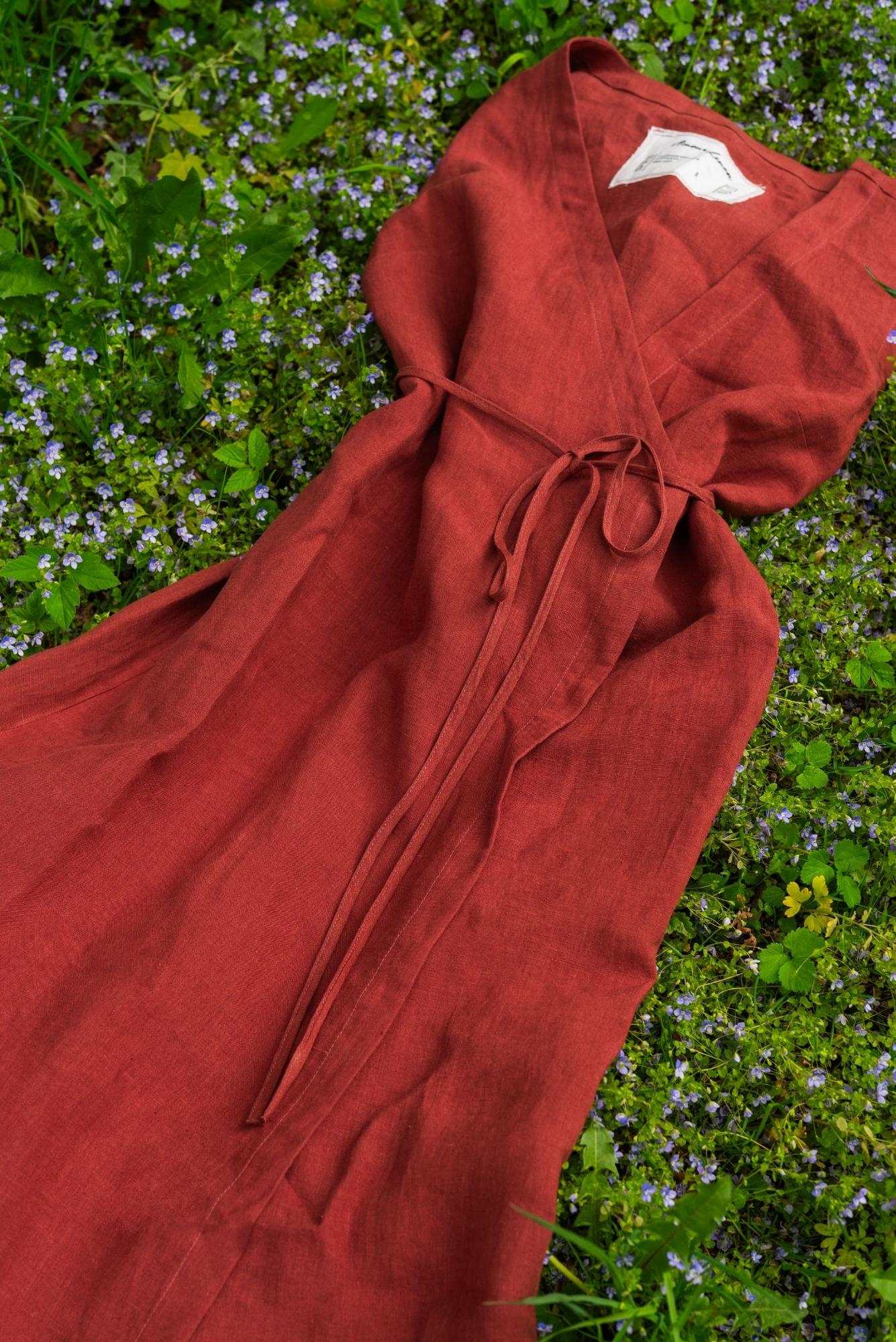 Rust-colored linen wrap dress from Amourlinen lying on grass with wildflowers